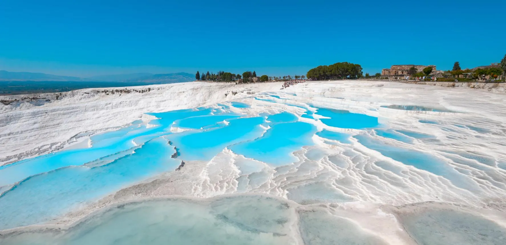 Turquoise pools on the white travertine terraces of Pamukkale under a blue sky